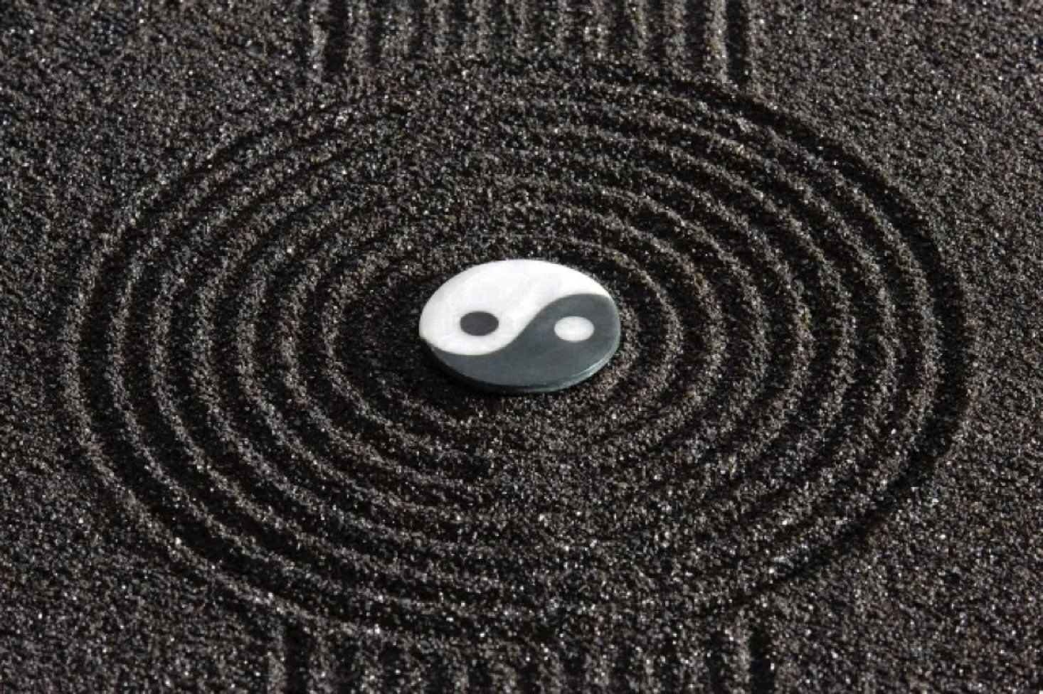 Yin-Yang-Symbol auf schwarzem Sand mit konzentrischen Kreisen.