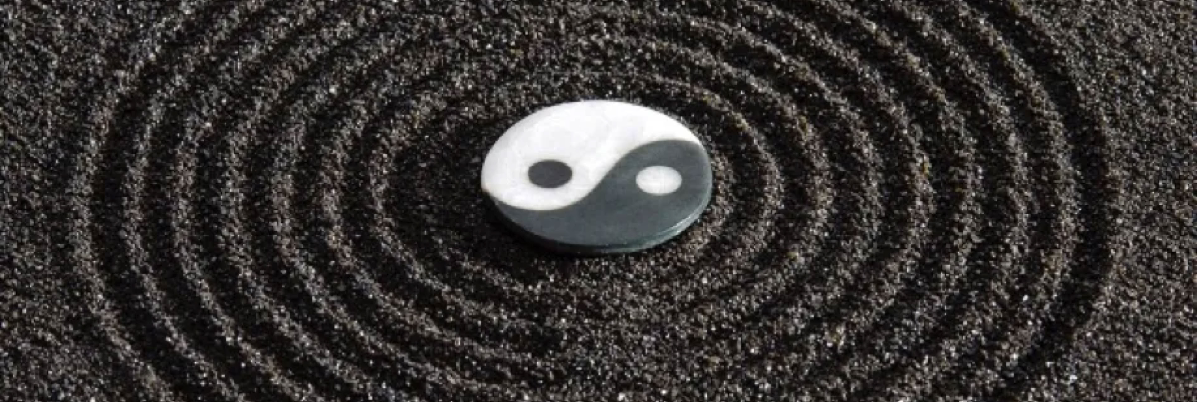 Yin-Yang-Symbol auf schwarzem Sand mit konzentrischen Kreisen.